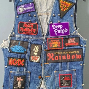 Pode incluir: Um colete de ganga azul com vários patches de bandas, incluindo Iron Maiden, AC/DC, Deep Purple, Rainbow e Van Halen. O colete é adornado com rebites prateados e tem uma etiqueta Wrangler.