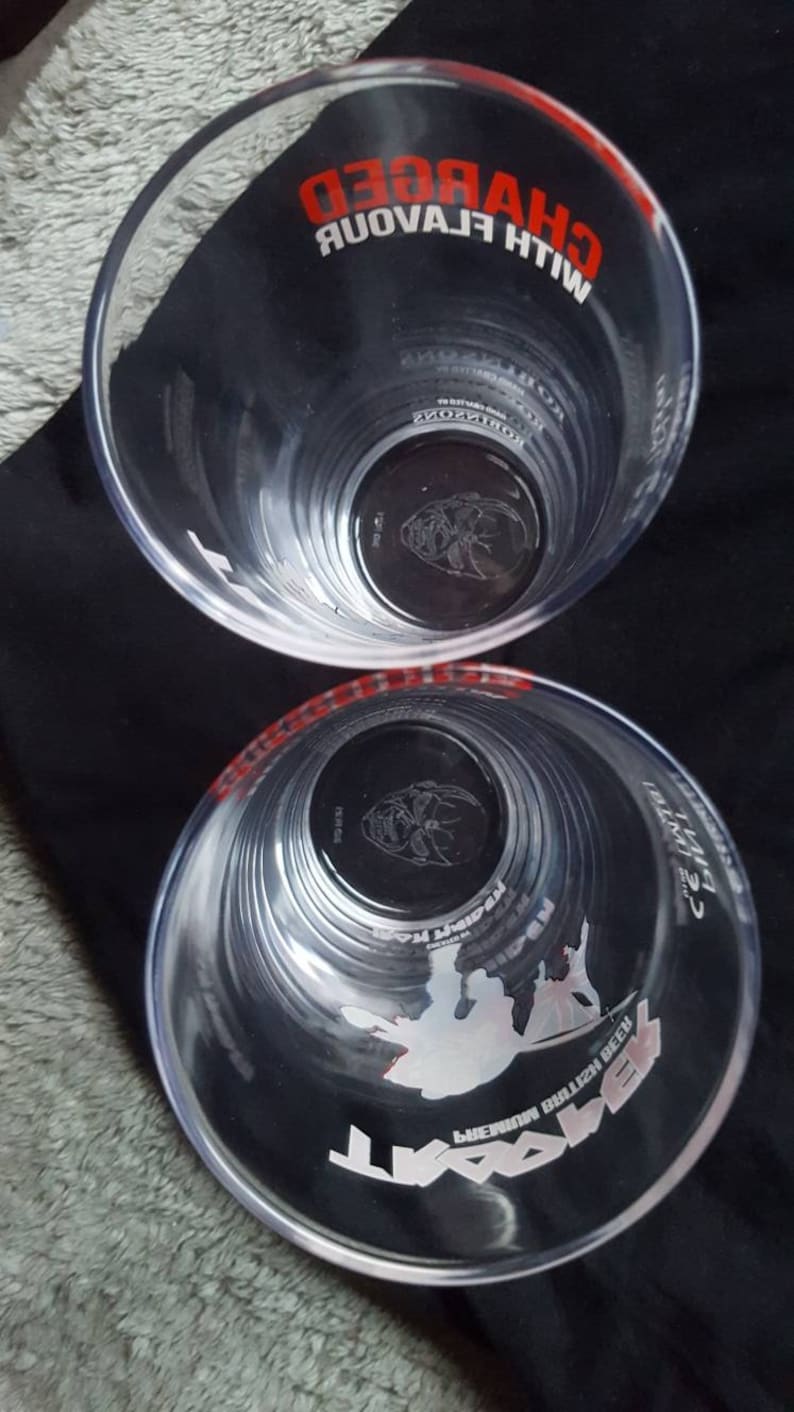 Puede incluir: Dos vasos de pinta de pl&aacute;stico transparente con gr&aacute;ficos en blanco y negro. El vaso superior tiene el texto "WITH FLAVOUR CHARGED" en rojo. El vaso inferior tiene el texto "PREMIUM BULLEN BEECH" y "WATT" en blanco.