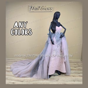 Puede incluir: Un vestido formal en un maniqu&iacute;, con un corpi&ntilde;o sin tirantes y una falda fluida con una larga cola. El vestido es principalmente rosa con acentos grises y de tul. El texto "ANY COLORS" se muestra a la izquierda.