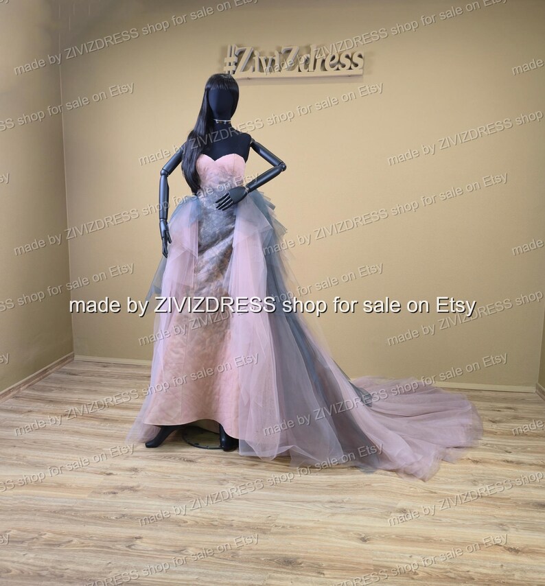 May include: A strapless, floor-length gown on a mannequin. The dress features a pink bodice and a layered skirt with gray and pink tulle. The train extends behind the mannequin. The mannequin is black and has long black hair.