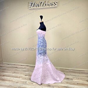 May include: A strapless, floor-length gown on a mannequin. The dress features a gradient design, transitioning from a light pink at the bottom to a blue and white pattern in the middle, and back to pink at the top. The text "#ZiviZdress" is visible.