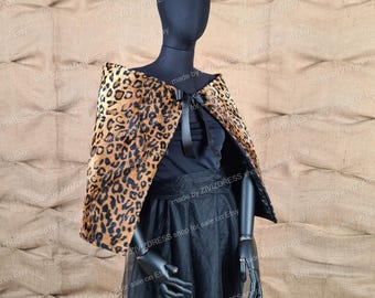 Könnte beinhalten: Ein brauner und schwarzer Leopardenfell-Imitat-Umhang mit einer schwarzen Satin-Schleife. Der Umhang wird über einem schwarzen Kleid mit schwarzem Tüll-Überzug getragen.