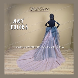May include: A formal gown on a mannequin with a long train. The dress has a layered design in grey and pink, with a large bow at the waist. The text "ANY COLORS" is visible. The dress is suitable for special occasions.