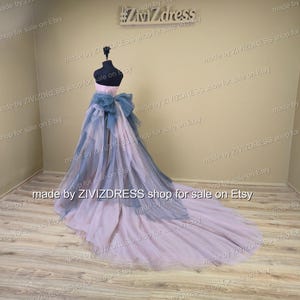 May include: A formal gown displayed on a mannequin. The dress has a pink bodice, a blue bow, and a layered skirt that fades from blue to pink. The train trails across the floor. The text "made by ZIVIZDRESS shop for sale on Etsy" is visible.