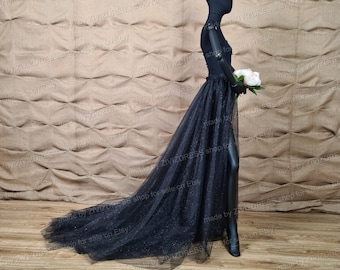 May include: A black tulle skirt with a sparkly overlay and a high slit. The skirt is worn over a black top and has a long train.