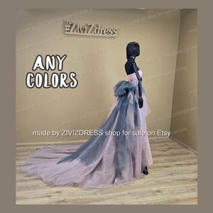 May include: A strapless, floor-length gown on a mannequin. The dress features a pink bodice, a large blue-gray bow, and a flowing train that transitions from pink to blue-gray. The text "ANY COLORS" is visible.
