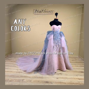 May include: A strapless, floor-length gown in shades of pink, blue, and white is displayed on a mannequin. The dress features a sweetheart neckline and a layered skirt with a long train. The text "ANY COLORS" is visible.