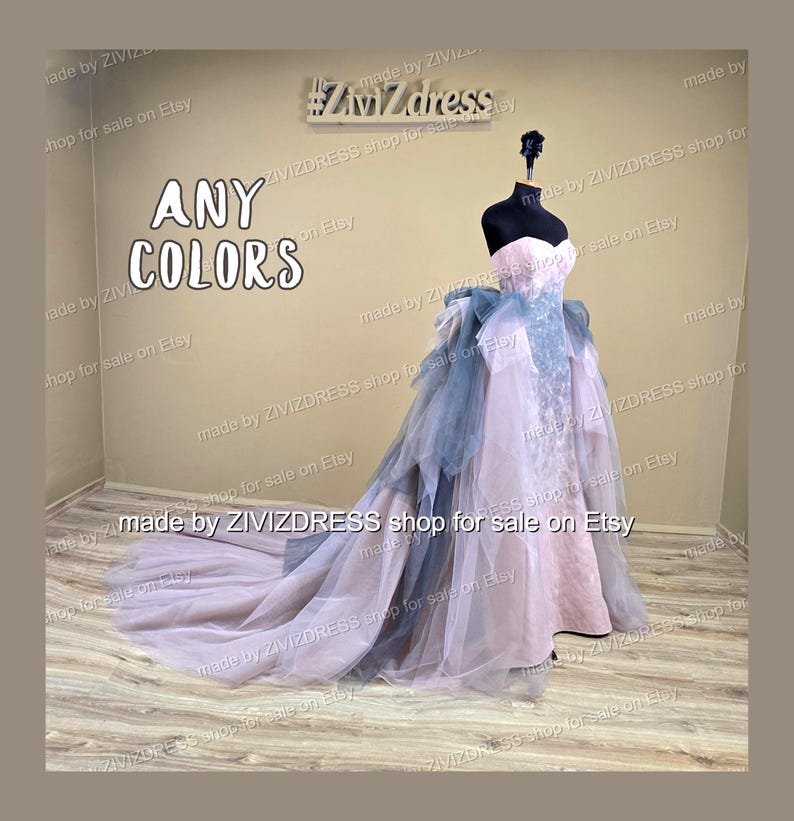 May include: A strapless, floor-length gown on a mannequin. The dress features a pink bodice, a blue sash, and a layered skirt with a long train. The text "ANY COLORS" is displayed in large letters. The dress is displayed in a shop.
