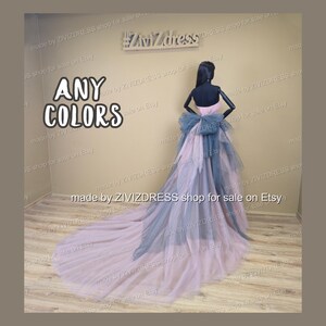 May include: A formal gown in shades of pink and blue, displayed on a mannequin. The dress features a layered skirt and a large bow at the back. The text "ANY COLORS" is visible.