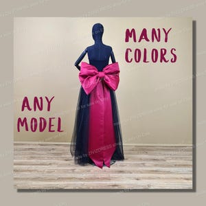 Puede incluir: Una falda de tul negro con una faja de satén fucsia y un gran lazo de satén fucsia. La falda está en un maniquí. El texto "ANY MODEL" está en el lado izquierdo de la imagen y el texto "MANY COLORS" está en el lado derecho de la imagen.