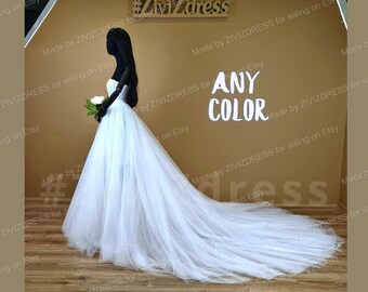Puede incluir: Un vestido de novia de tul blanco con una larga cola. El vestido está en un maniquí en un entorno de tienda. El letrero sobre el vestido dice "ANY COLOR".