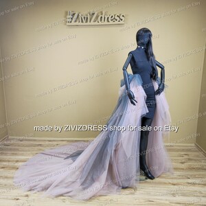 May include: A black dress with a high-low tulle skirt in shades of pink and grey is displayed on a mannequin. The dress has a fitted bodice and a flowing, layered skirt that extends into a long train. The mannequin is black.