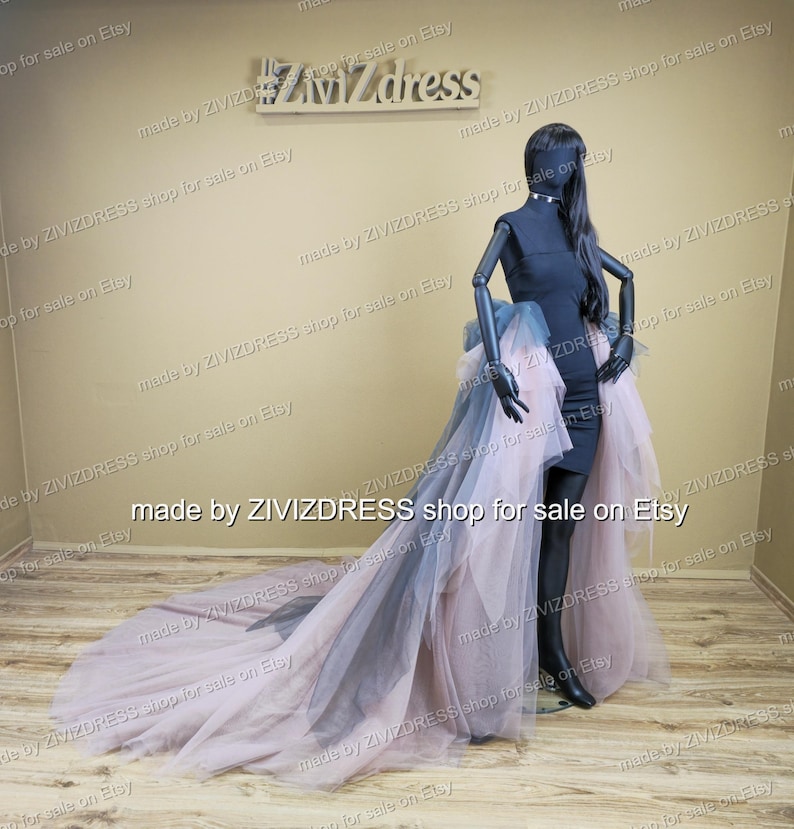 May include: A black dress with a high-low tulle skirt in shades of pink and grey is displayed on a mannequin. The dress has a fitted bodice and a flowing, layered skirt that extends into a long train. The mannequin is black.