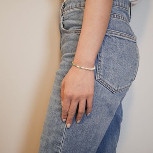 May include: A close-up of a person's wrist wearing a multi-colored beaded bracelet with white pearls.