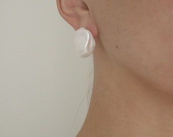 May include: A pair of white pearl earrings. The earrings are round and have a slightly irregular shape. They are a classic and elegant style.