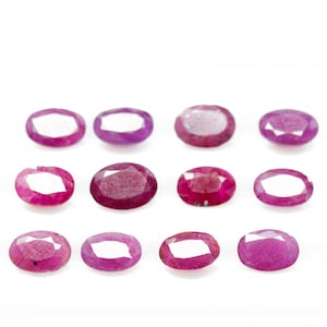 May include: Twelve oval-shaped gemstones, all a vibrant pink-red color, are arranged in three rows of four on a white background.