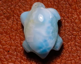 Könnte beinhalten: Ein blauer und weißer geschnitzter Schildkrötenanhänger aus Ozeanjaspis. Der Anhänger hat eine glatte, polierte Oberfläche und ist ein wunderschönes Beispiel für diesen einzigartigen Edelstein.