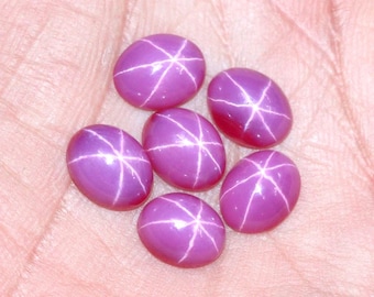 May include: Six pink star ruby gemstones with a star-like pattern in the center of each stone.