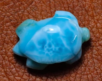 Könnte beinhalten: Eine geschnitzte, hellblaue Edelstein-Schildkrötenfigur. Die Schildkröte hat eine glatte, polierte Oberfläche mit weißen Marmorierungen. Der Edelstein hat eine leuchtende türkise Farbe mit einem Hauch von Grün an den Flossen und am Kopf. Die Schildkröte ist ein kleiner, dekorativer Gegenstand.