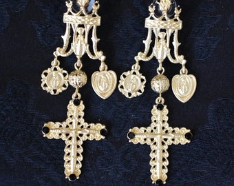 May include: A pair of gold-tone dangle earrings with black accents. Each earring features a cross charm with black stones, a ball charm, and three charms with religious imagery.