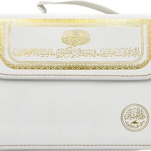 Puede incluir: Estuche rectangular blanco con detalles decorativos dorados y escritura &aacute;rabe. El estuche tiene un asa y un borde cosido. Un emblema dorado se encuentra en la esquina inferior derecha.