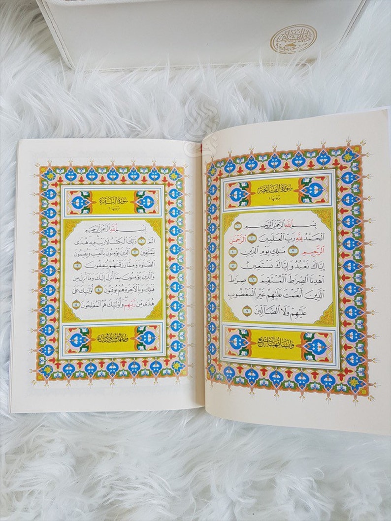 Puede incluir: Un libro abierto con bordes ornamentados y coloridos y escritura &aacute;rabe. Las p&aacute;ginas son de color crema y el texto es negro. El libro es probablemente un texto religioso, posiblemente el Cor&aacute;n, con caligraf&iacute;a detallada.