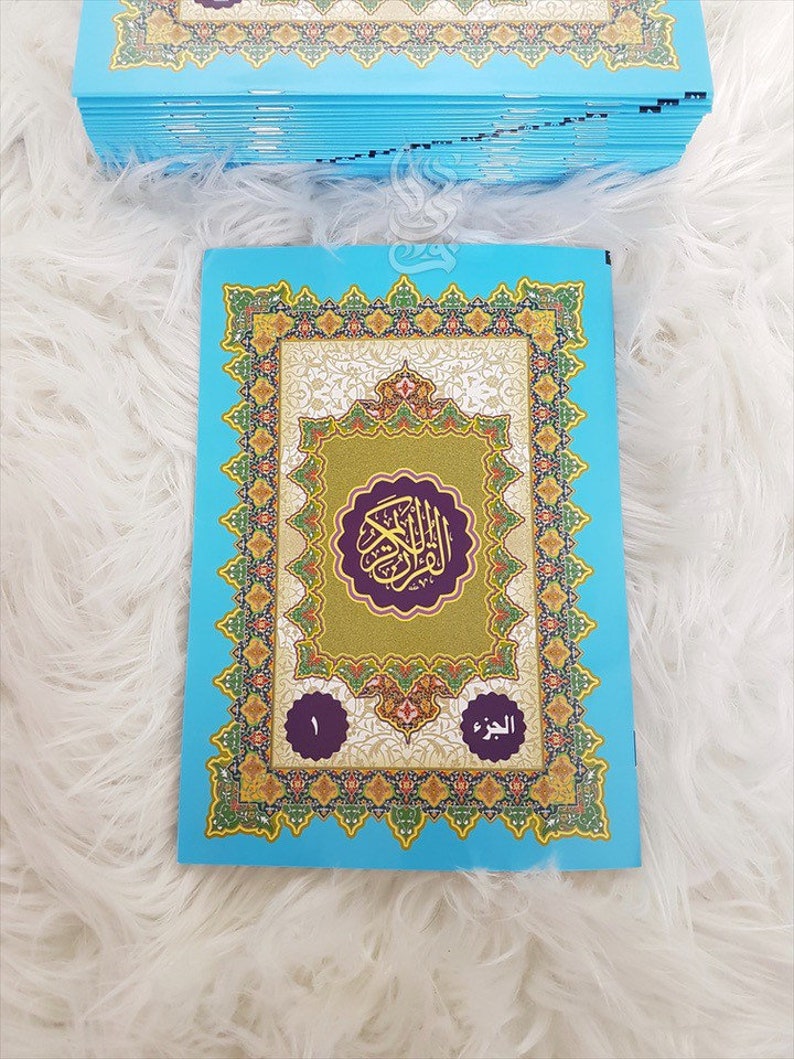 Puede incluir: Una pila de libros azul claro con cubiertas ornamentadas y coloridas. La portada del libro superior presenta dise&ntilde;os dorados, verdes y morados con texto &aacute;rabe. El libro est&aacute; etiquetado con el n&uacute;mero 1 y texto &aacute;rabe.