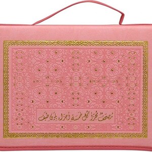 Puede incluir: Malet&iacute;n de transporte rosa con asa. La funda presenta un dise&ntilde;o floral en relieve con ribete dorado y texto. La funda rectangular tiene un asa en la parte superior. El dise&ntilde;o es ornamentado y decorativo.