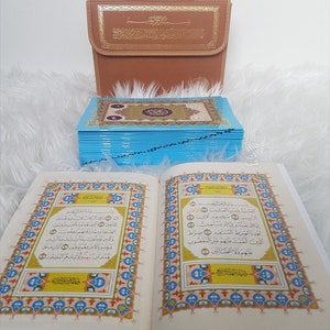 Puede incluir: Un libro abierto con bordes ornamentados y coloridos y escritura &aacute;rabe se muestra, junto a una pila de p&aacute;ginas con bordes azules y un estuche de transporte marr&oacute;n con letras doradas. El libro est&aacute; abierto en una p&aacute;gina con caligraf&iacute;a detallada.