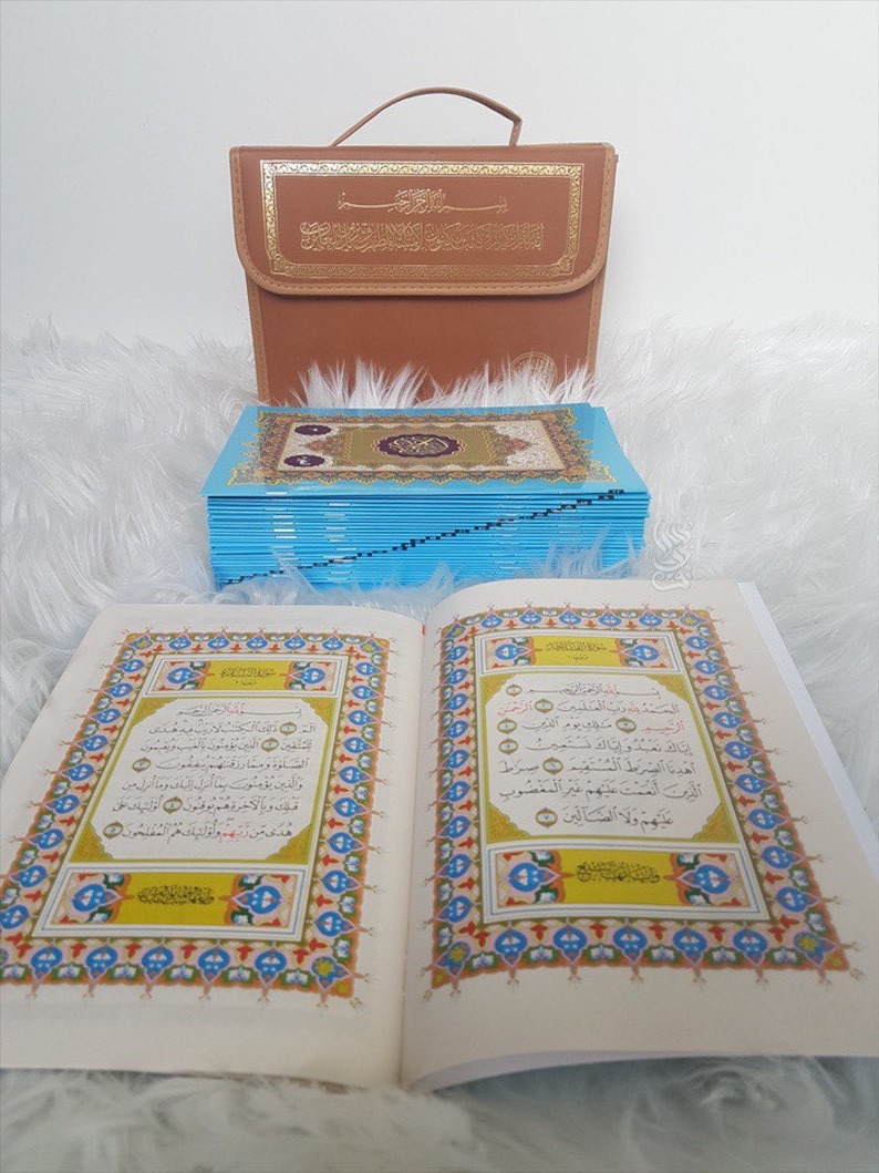 Puede incluir: Un libro abierto con bordes ornamentados y coloridos y escritura &aacute;rabe se muestra, junto a una pila de p&aacute;ginas con bordes azules y un estuche de transporte marr&oacute;n con letras doradas. El libro est&aacute; abierto en una p&aacute;gina con caligraf&iacute;a detallada.