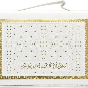 Puede incluir: Cubierta de libro rectangular blanca con un dise&ntilde;o floral dorado y un borde dorado. La cubierta tiene un asa en la parte superior. El texto de la cubierta est&aacute; en &aacute;rabe.