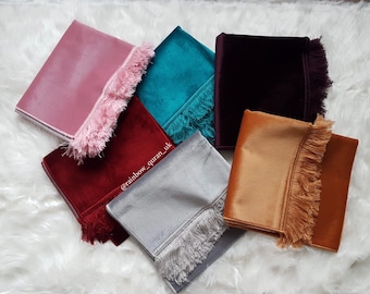 Op de afbeelding: Zes verschillende gebedskleden met franjes. De kleden zijn in de kleuren roze, turquoise, bordeauxrood, rood, grijs en oranje.