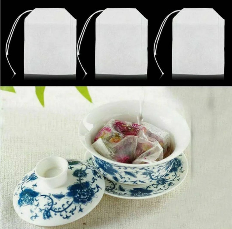 May include: Three white tea bags, made of fine mesh fabric, are shown against a black background. The tea bags are empty, but one is shown in a white porcelain teacup with a blue and white floral design, filled with water and loose tea leaves.
