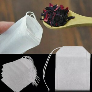 May include: A pack of 10 white tea bags with a drawstring. The tea bags are made of a fine mesh material and are perfect for loose leaf tea. The tea bags are shown next to a spoon filled with dried hibiscus flowers.