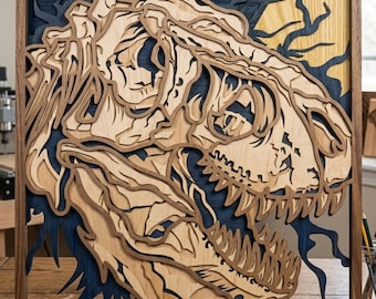 Pode incluir: Uma obra de arte em madeira em camadas com um crânio de Tyrannosaurus Rex detalhado. A obra de arte usa vários tons de marrom e tons de madeira natural, em um fundo azul escuro dentro de uma moldura de madeira. O design destaca os dentes e a estrutura óssea.