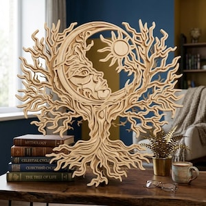 Peut inclure: Une œuvre d'art murale en bois superposé représentant un arbre avec un croissant de lune et un soleil. L'œuvre est en bois clair et présente des détails complexes. Elle est exposée sur une table en bois avec des livres et une tasse à café.