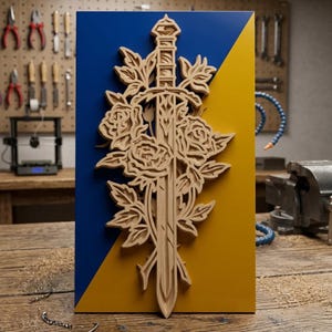 Könnte beinhalten: Ein Holzrelief mit einem Schwert, das von Rosen und Blättern umgeben ist, vor einem blau-gelben Hintergrund. Das Kunstwerk ist aus hellem Holz gefertigt und zeigt detaillierte florale und Klingen-Elemente. Der Hintergrund ist diagonal geteilt.