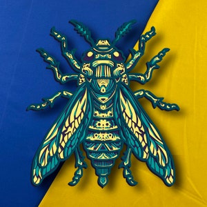 May include: A blue and yellow intricate paper cut-out of a bee with detailed wings and a patterned body.