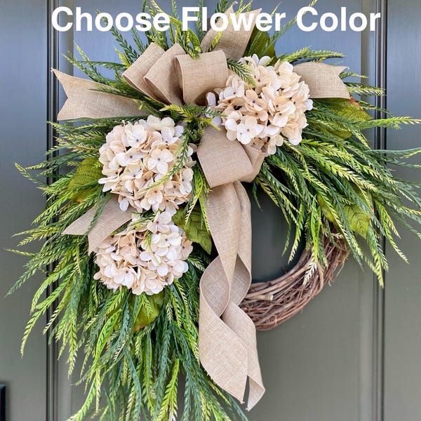 May include: A wreath with a burlap bow and cream-colored hydrangea flowers. The wreath is made of grapevine and has a green leafy base. The text "Choose Flower Color" is visible at the top of the image.