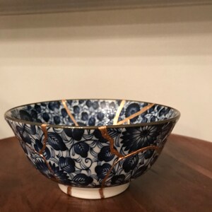 May include: A blue and white ceramic bowl with a floral pattern and gold cracks. The bowl is sitting on a wooden surface.