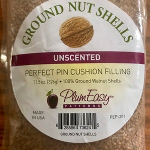 May include: A bag of 11.5 oz (326g) of unscented ground walnut shells for pin cushion filling. The bag is labeled "PlumEasy Patterns" and has a barcode. The text "GROUND NUT SHELLS" is printed on the bag.