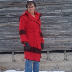 Puede incluir: Una chaqueta roja con capucha, ribetes negros y cinturón. La chaqueta se lleva sobre unos vaqueros azules.