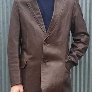 以下が含まれることがあります： 2つのボタン留めと2つのフロントポケットが付いたブラウンの革のブレザーです。