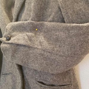 Puede incluir: Una chaqueta gris de espiga con un cierre de botón único y un bolsillo en el lado izquierdo.