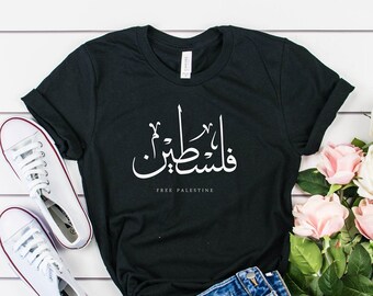 May include: A black t-shirt with the Arabic phrase "Free Palestine" in white lettering. The shirt is paired with blue denim shorts and white sneakers. A bouquet of pink and white roses is in the background.