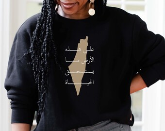May include: Black sweatshirt with a tan outline of the Palestinian territories and Arabic text that reads "On this land, we were born, we will live, we will resist, we will return."
