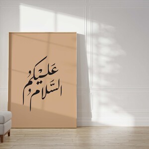 May include: A beige framed poster with black Arabic calligraphy that reads "عليكَ و علينا" which translates to "On you and on us".