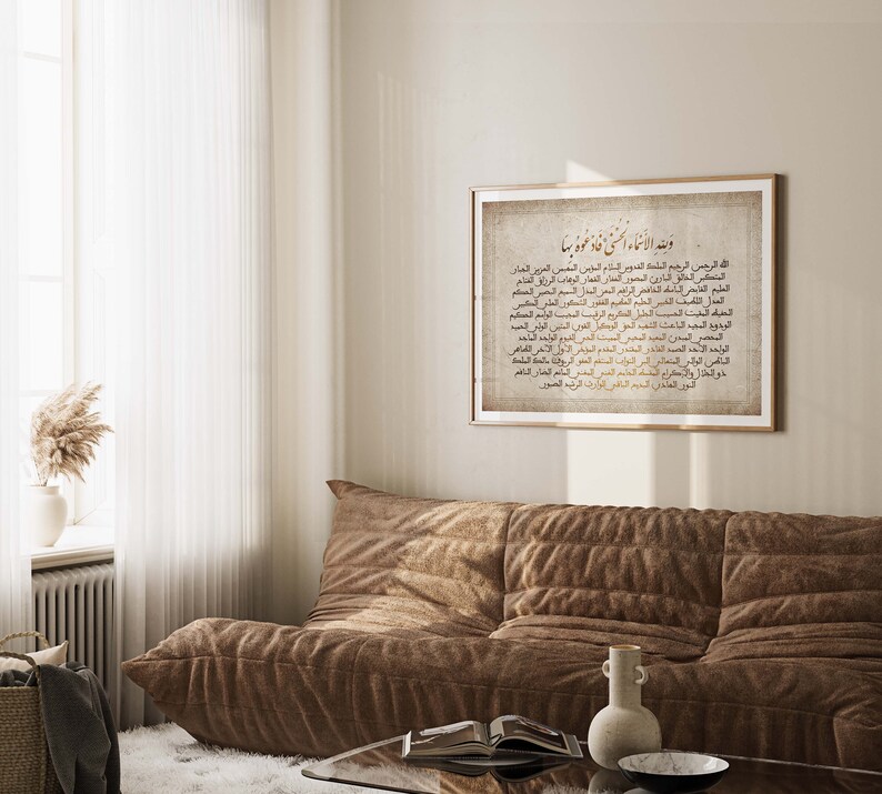 May include: A framed print with a beige background and gold Arabic calligraphy. The text is a list of the 99 names of Allah, also known as the Asma ul Husna. The print is hanging on a light beige wall above a brown couch.