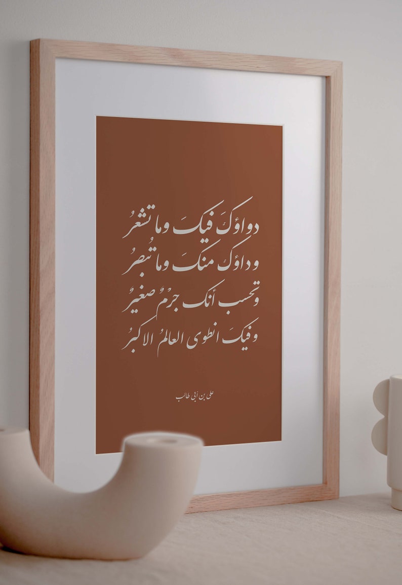 May include: A framed print with a brown background and white Arabic calligraphy. The text reads "Dawa'uk fiik wa ma tash'ur, wa da'uk ming wa ma tubsir, wa tahsib annaka jirm jism saghir, wa fiik an'tawi al-'alam al-akbar." The text is attributed to "Ali ibn Abi Talib".