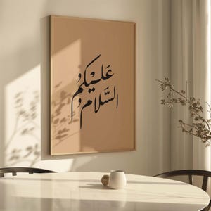 May include: A framed print with a beige background and black Arabic calligraphy that reads "Salam wa alaikum" in a modern font style.